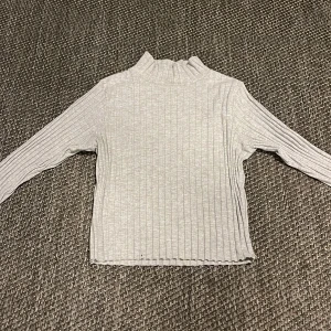 Grå ribbad polotröja från CHIC - Säljer en stilren grå polotröja från CHIC. Den är ribbad och har långa ärmar, perfekt för kyligare dagar. Tröjan är i ett mjukt och bekvämt material som passar både till vardags och lite finare tillfällen.