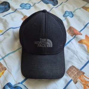 Svart keps från The North Face - Säljer en snygg svart keps från The North Face. Den har en klassisk design med justerbar rem baktill för perfekt passform. Perfekt för både vardag och utomhusaktiviteter!