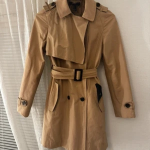 Trench coat - Jättefin medellång trench coach. Liten defekt där det lossnat lite vid axeln men det går enkelt att sy upp.