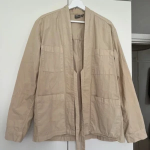 Beige kappa med knyte - Beige overshirt eller beige kort kappa med snörning knyte rosett och fickor 