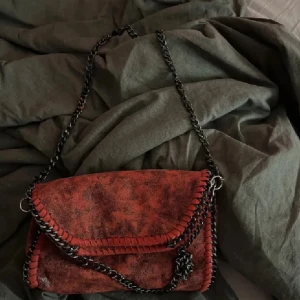 Röd axelväska med kedja - Säljer en supercool röd axelväska med kedjedetaljer. Väskan har en unik design med snygga sömmar och en kedja som axelrem. Perfekt för att ge din outfit en edgy touch! 🖤pris kan diskuteras! 