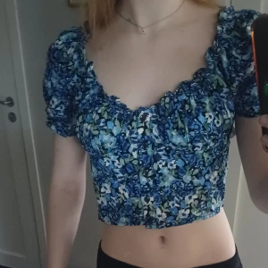 Blommig croppad topp - Säljer en jätte söt blommig croppad topp med ett jätte fint blommigt mönster. Toppen har korta puffärmar och en v-ringning med volangdetaljer. Har använt den ett fåtal gånger och toppen har en väldigt fin passform💕💗