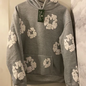 Grå hoodie från Denim Tears - Säljer denna denim tears hoodie som är helt ny, jag säljer den för att den är stor på mig. Den är såklart äkta. Fick den i present av pappa. Han köpte den för ett tag sedan men han gömde den så han skulle ge mig den som present. Men han köpte den stor för att han trodde jag skulle växa mycket i denna tiden men det gjorde jag inte 😅 Det står att den är m i storleken men den passar både för m och l. Den är jättevarm och man känner sig mycket bekväm i den. Jag kan gå ner i priset vid snabb affär. 