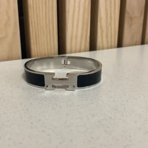 Svart och silver H armband - Elegant armband i svart och silver med en stilren design. Armbandet har en distinkt H-formad detalj i mitten som ger det en modern touch. Perfekt för att komplettera en stilren look. Kan gå ner i pris. ✌️den låser sig inte riktigt men det är bara att skruva till den lite.