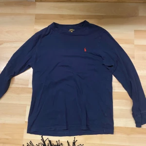 Mörkblå långärmad tröja från Ralph Lauren - Säljer en stilren mörkblå långärmad tröja från Ralph Lauren med det klassiska röda broderade logotypen på bröstet. Perfekt för en avslappnad och snygg look. Tröjan är i storlek XL och har en bekväm passform.
