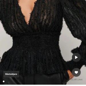 Svart blus från NA-KD - Säljer en elegant svart blus från NA-KD med en djup v-ringning och långa ärmar. Blusen har en unik textur med fransiga detaljer och en smockad midja som ger en fin passform. Perfekt för att lyfta vilken outfit som helst! Använd 1 gång och nypris ligger på 449kr