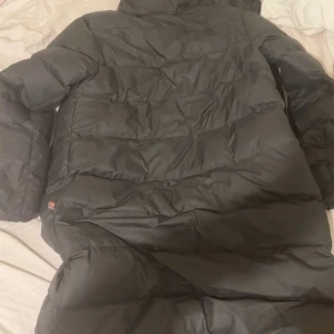 Svart dunjacka från Nike - Säljer en svart dunjacka från Nike med Storm-FIT teknologi. Jackan har en dragkedja framtill och är långärmad. Perfekt för kyliga dagar med sin pufferdesign som håller värmen inne.