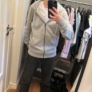 Grå hoodie från Jack & Jones - Säljer en stilren grå hoodie från Jack & Jones. Den har dragkedja framtill och en praktisk huva med snörning. Perfekt för en avslappnad stil. Har knappt använt, nästan som ny. Säljer eftersom den är för stor. Passar  165-170.