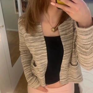 Beige och svart randig kavaj - Snygg beige och svart randig kavaj med långärmad design. Perfekt för en stilren look. Kavajen har en öppen front utan knappar och är tillverkad i ett mjukt material.