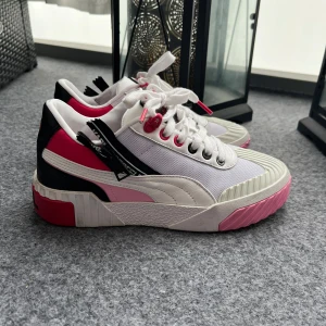 Puma x Karl Lagerfeld sneakers - Snygga sneakers från Puma i samarbete med Karl Lagerfeld. Skorna har en fräsch vit bas med rosa och svarta detaljer. De är utrustade med snörning och har en unik design med 'KARL' text på hälen.