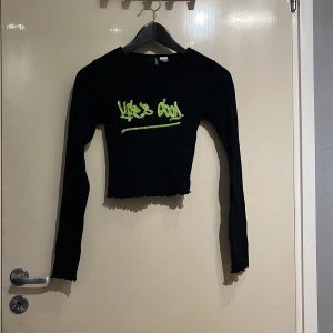 Svart långärmad topp från H&M - Säljer en svart långärmad topp från H&M med texten 'Life's Good' i neonfärg på framsidan. Toppen är croppad och har en ribbad kant vid nederdelen. Perfekt för en cool och avslappnad stil.