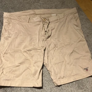 Beige shorts från Gant - Snygga beige shorts från Gant med knapp och dragkedja framtill. De har en klassisk design med två bakfickor med knappar och en liten broderad logga på framsidan. Perfekta för en avslappnad stil. Står ingen stl men gissar på Xl-Xll+ skriv för mått. Jätte snygga och sköna för sommaren! Pris kan alltid diskuteras och skriv till mig för övriga frågor eller bilder!