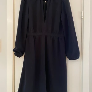 Svart klänning med v-ringning By Malina strl S - Elegant svart klänning med djup v-ringning och långa ärmar. Perfekt för en stilren look. Klänningen har en klassisk design som passar många tillfällen. Ny svart klänning i strl S från By Malina.  Klänningen har en underklänning.  Ny, aldrig använd.  Mått Över bröstet: ca 46 cm Längd från axeln och ner: ca 98 cm  50% bomull och 50% polyester   Kommer från ett djur och rökfritt hem.