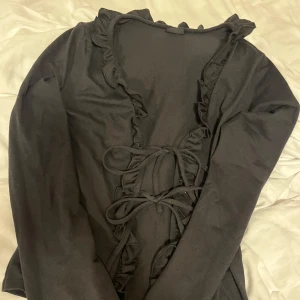 Svart långärmad topp från Gina Tricot - Säljer en svart långärmad topp från Gina Tricot med volangdetaljer och snörning framtill. Perfekt för en stilren look. Passar bra till både jeans och kjol. 🖤