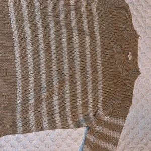 Beige och vit randig stickad tröja från Kilky - Säljer en mysig beige och vit randig stickad tröja från Kilky. Tröjan har långa ärmar och en rund halsringning. Perfekt för kyligare dagar och ger en avslappnad stil.