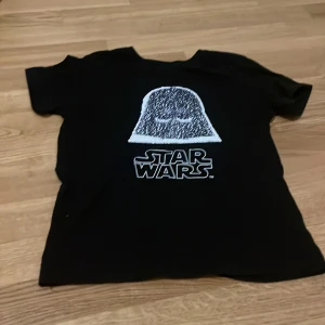 Svart Star Wars t-shirt - Cool svart t-shirt med Star Wars-tryck på framsidan. Perfekt för unga fans av galaxens äventyr. T-shirten har korta ärmar och är gjord i ett bekvämt material.