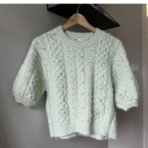 Ljusgrön stickad tröja från Zara, slutsåld  - Säljer en ljusgrön stickad tröja från Zara med korta ärmar med vita pärlor på. Tröjan har en rund halsringning och ribbade kanter. Aldrig använd, nypris 399kr