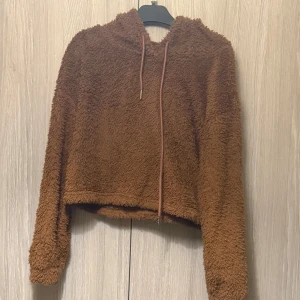 Brun fluffig hoodie - Mysig brun hoodie med fluffigt material och huva. Perfekt för kyliga dagar. Den har långa ärmar och en croppad passform som ger en trendig look.