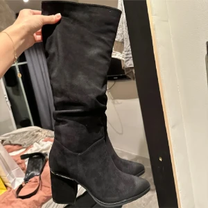 Svarta mockastövlar med klack - Snygga svarta stövlar i mocka med hög klack. Perfekta för att ge en elegant touch till din outfit. De har en klassisk design som passar till många olika stilar.