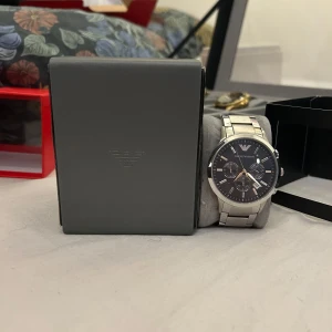 Silverfärgad klocka från Emporio Armani - Stilren klocka från Emporio Armani med silverfärgad länk och svart urtavla. Klockan har tre mindre urtavlor och tydliga visare. Perfekt för den som vill ha en elegant accessoar. Pris kan diskuteras 
