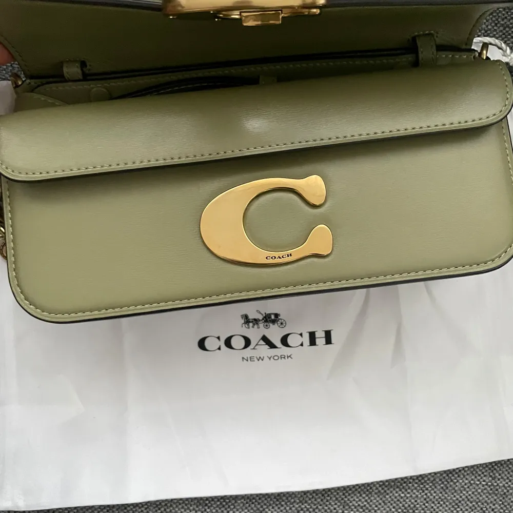 Snygg olivgrön axelväska från Coach i skinn med guldfärgad kedja och spänne. Väskan har en elegant design med ett praktiskt inre fack och en justerbar rem. Perfekt för att ge din outfit en stilfull touch. Ordinarie pris 6400kr. Helt ny och oanvänd alla prislappar sitter kvar , en dustbag följer med. Skicka prisförslag .. Laukut & Käsilaukut.