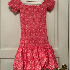 Rosa kortklänning med volangdetaljer - Säljer en söt rosa kortklänning med ett livligt mönster och volangdetaljer vid fållen. Klänningen har korta ärmar och en smickrande passform som är perfekt för sommarens äventyr. Perfekt för dig som vill sticka ut med stil! 🌸