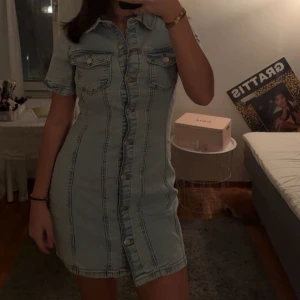 Helt ny Jeansklänning - Trendig jeansklänning i ljus denim med knappar framtill och korta ärmar. Klänningen är helt ny med prislapp på köptes för 599, storlek 38. Klänningen har en figurnära passform som framhäver silhuetten.