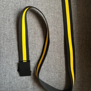 Svart och gult bälte med spänne - Snyggt bälte med svart och gult randigt mönster. Bältet har ett stilrent svart spänne och är perfekt för att ge en färgklick till din outfit. Passar både till jeans och andra byxor. Ca 110-120 cm. 