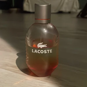 Lacoste Eau de Toilette 75ml - Säljer en Lacoste Eau de Toilette i en stilren flaska på 75 ml. Flaskan har en elegant design med en grå kork och den ikoniska Lacoste-loggan. Perfekt för den som vill ha en fräsch och sportig doft.