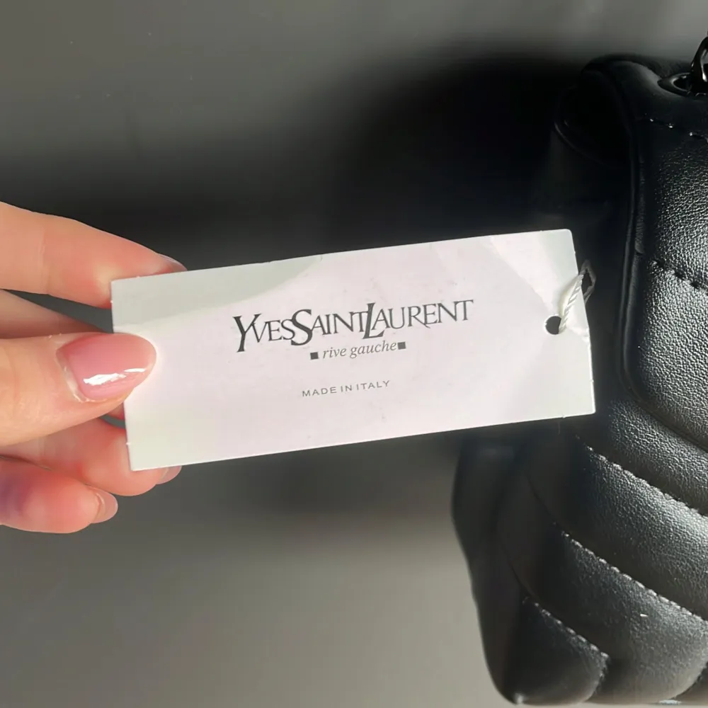Snygg svart axelväska från Saint Laurent med quiltad design och kedjeaxelrem. Väskan har en elegant YSL-logga på framsidan. Perfekt för att ge din outfit en lyxig touch. Pris kan diskuteras, den är inte äkta!. Laukut & Käsilaukut.