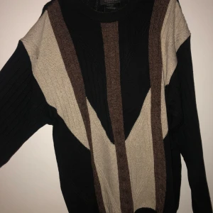 Mjuk tröja från Tosani - Säljer en snygg randig tröja från Tosani i svart, beige och brun. Tröjan är tillverkad i en blandning av bomull, ull och akryl, vilket gör den både bekväm och varm. Perfekt för kyligare dagar! Köptes från beyond retro, och därefter inte använd i min ägo.
