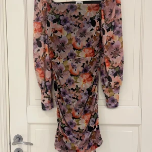 Blommig klänning med långa ärmar - Säljer en färgglad blommig klänning med långa ärmar och rynkade detaljer. Klänningen har en vacker mix av lila, rosa, orange och gröna toner. Perfekt för en somrig look!