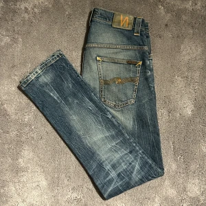 Nudie jeans, Modell: Thin Finn - Snygga blå jeans i modell Thin Finn från Nudie Jeans med en klassisk femficksdesign och slitna detaljer. 