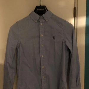 Blå skjorta från Ralph Lauren - Skick 10/10 aldrig användSnygg blå skjorta från Ralph Lauren i slim fit. Skjortan har långa ärmar och knappar framtill samt en broderad logotyp på bröstet. Perfekt för en stilren look.