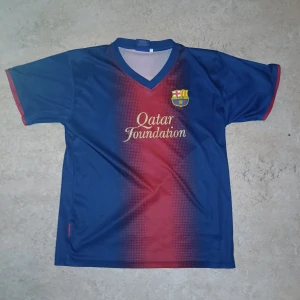 Blå och röd FC Barcelona fotbollströja Frakten kostar 25kr - Säljer en blå och röd FC Barcelona fotbollströja med korta ärmar. Tröjan har Qatar Foundation-logga på framsidan och Messi 10 tryckt på baksidan. Perfekt för fans av laget och spelaren! 