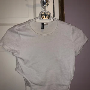 Vit ribbad topp från H&M Divided - Säljer en vit ribbad topp från H&M Divided. Toppen har korta ärmar och en rund halsringning. Perfekt för en stilren och enkel look. Passar bra till jeans eller kjol. Knyt ihop på sidan. Skulle säga att den är mer åt Xs hållet