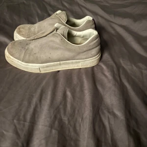 Grå sneakers i mocka(EYTYS) - Säljer ett par grå sneakers i mocka med en stilren design utan snörning. Skorna har en vit sula och en diskret dragflik baktill. Perfekta för en avslappnad stil.