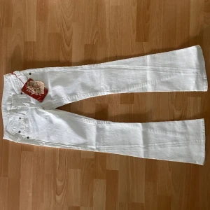  True Religion super låga  - Snygga vita jeansbyxor från True Religion med klassisk femficksdesign och knappgylf. Perfekta för en stilren look. Märkets logga syns på knappen och etiketten. Dom är väldigt låga och skitsnygga verkligen de finns en super liten blå fläck på låret men det syns inte 
