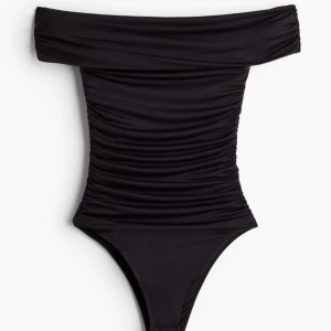Svart off-shoulder body - Trendig svart body med off-shoulder design och rynkade detaljer. Den har en elegant passform som framhäver figuren. Ny med prislapp kvar
