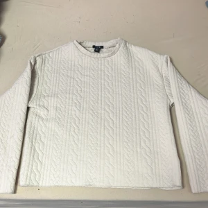 Vit stickad tröja från Amisu/New Yorker - Säljer en stilren beige stickad tröja från Amisu. Tröjan har ett klassiskt flätmönster och långa ärmar, perfekt för kyligare dagar. Den är både bekväm och snygg, ett måste i garderoben!