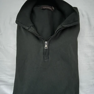 Mörkgrön halz-zip Oscar Jacobson - Snygg mörkgrön tröja från Oscar Jacobson med dragkedja vid halsen. Perfekt för en stilren look. Tröjan har långa ärmar och ribbade muddar vid ärmslut och nederkant.