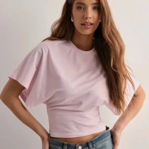 Ljusrosa kortärmad topp - Säljer en söt ljusrosa topp med korta ärmar och en tight passform i midjan. Perfekt för en avslappnad stil med jeans eller kjol. Toppen är gjord i ett mjukt material som känns skönt mot huden.