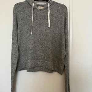 Grå hoodie från Hollister - Säljer en mysig grå hoodie från Hollister. Den har en croppad design med långa ärmar och en justerbar huva med vita snören. Perfekt för en avslappnad stil. 🩶