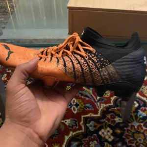 Orange och svarta fotbollsskor från Puma - Säljer ett par coola fotbollsskor från Puma i orange och svart. Skorna har snörning och en mönstrad design med dobbar för bra grepp på planen. Perfekta för fotboll, de är använda ett par gånger bara och är på top sick.