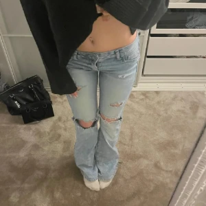Lågmidjade jeans med slitningar - Säljer ett par ljusa jeans med slitningar på knäna och låren. De har en bootcut-stil och är lågmidjade, super snygga🥰Midjemått: 32 Innerbenslängd : 72