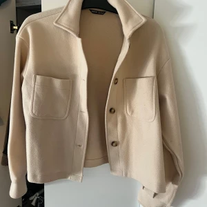 Beige jacka  - Säljer en stilren beige jacka med knappar framtill och två stora fickor. Jackan har en klassisk krage och långa ärmar, perfekt för en avslappnad look. Passar bra till både jeans och kjol.