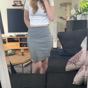 Grå kjol med dragkedja - Snygg grå kjol i normal passform med en cool dragkedja på sidan. Kjolen är knälång och perfekt för en stilren look. Den har en enkel design som gör den lätt att matcha med olika toppar. Asymmetrisk och lite omlott 