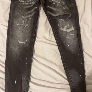 Svarta slitna jeans - Säljer ett par svarta jeans med slitningar och färgstänk för en cool och avslappnad look. Perfekta för dig som gillar en edgy stil. De har en straight passform och är tillverkade i jeansmaterial. Storleken är i barn så 33 motsvara 46-48