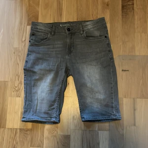 Grå jeansshorts från Garcia Jeans - Snygga grå jeansshorts från Garcia Jeans med klassisk femficksdesign. De har en knapp och dragkedja framtill samt en diskret logga på bakfickan. Perfekta för en avslappnad stil. 