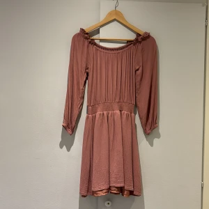 Rosa klänning från Bubbleroom - Säljer en söt rosa klänning från Bubbleroom i storlek XS. Klänningen har trekvartsärmar och en offshoulder-design med fina rynkdetaljer vid halsen. Perfekt för en avslappnad och stilfull look.